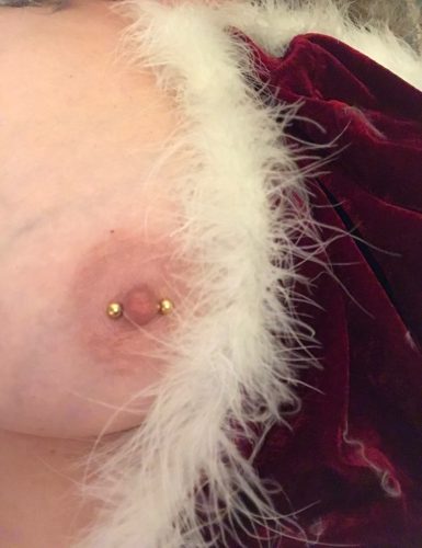 Close up of boob with pierced nipple half-covered with white fur and dark red velvet.